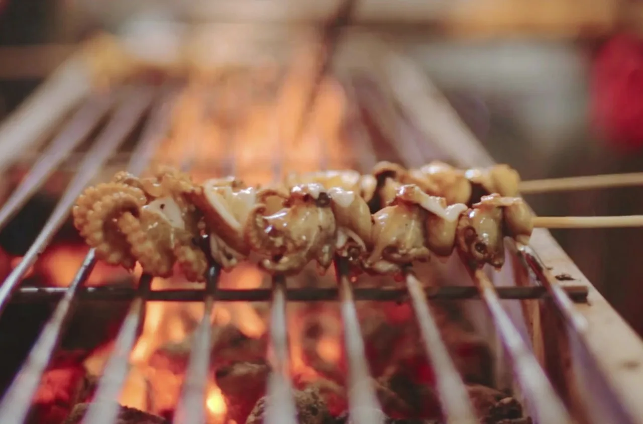 Skewers of grilled meat cooking over glowing charcoal