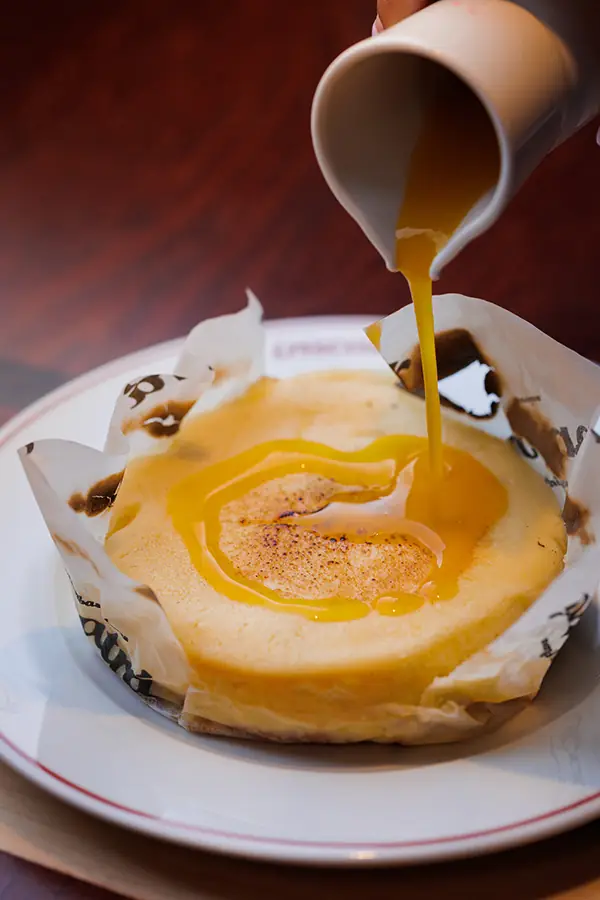 Citrus glaze being poured over a warm caramelized custard dessert wrapped in parchment paper, Tracatrá