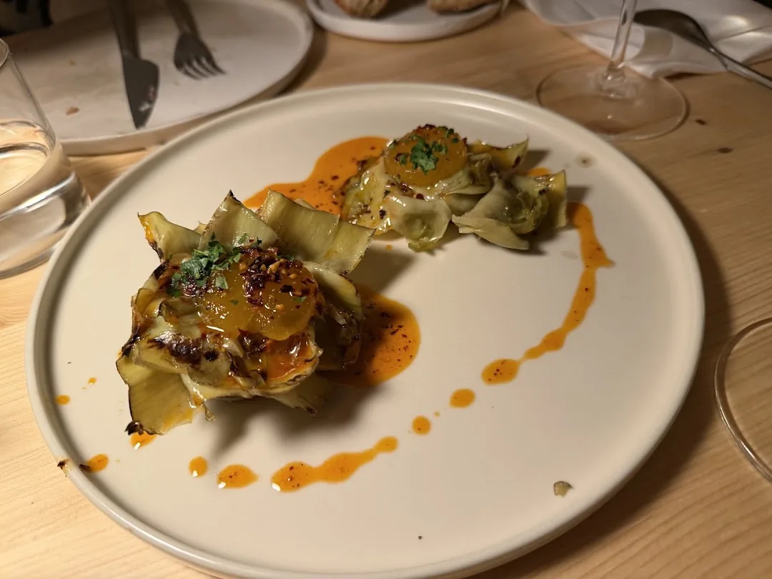 Two charred whole artichokes on a white plate drizzled with a spiced orange-red sauce