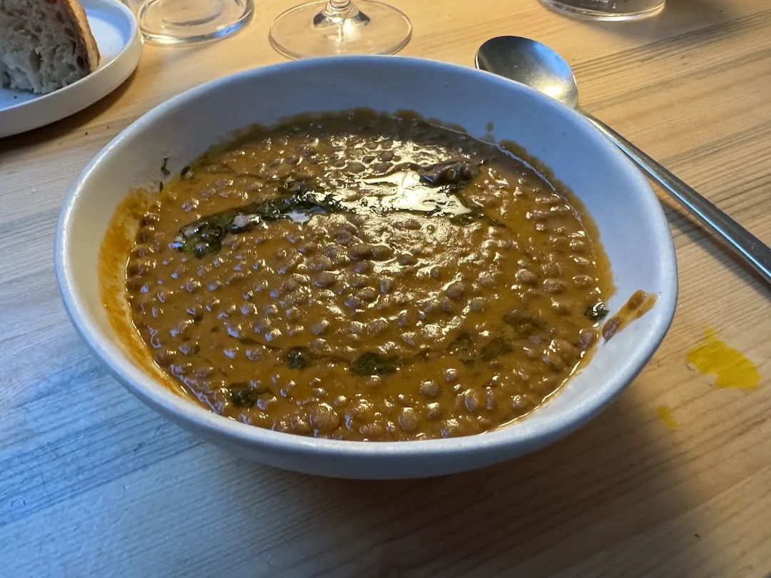 A bowl of creamy brown lentil stew with a herb garnish and drizzle of oil