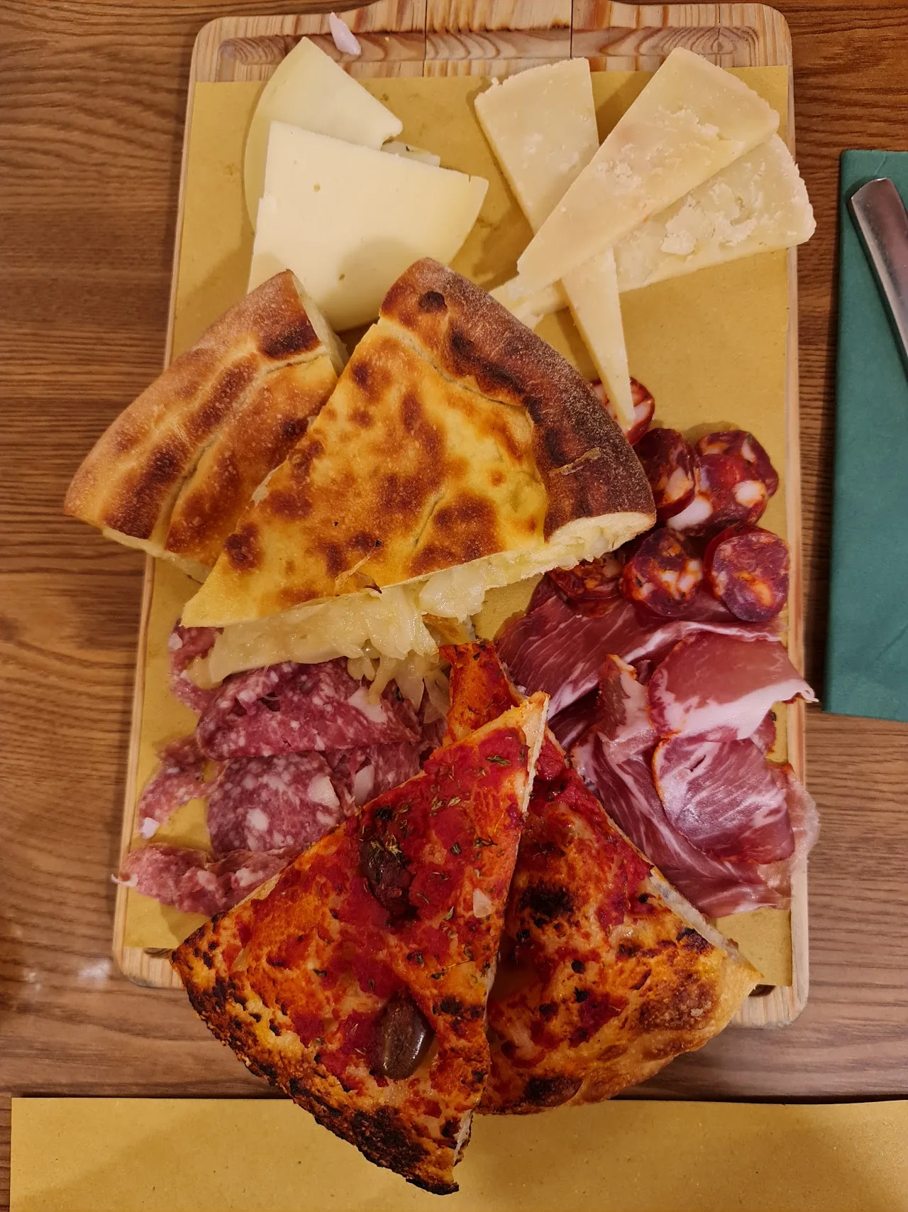 A wooden board with pizza slices, cheese, and cured meats
