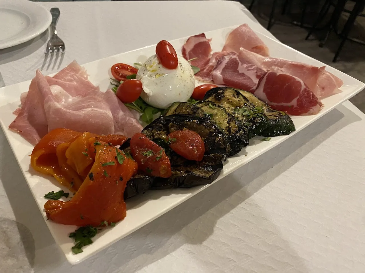 An antipasto plate with burrata, prosciutto, roasted vegetables, and cherry tomatoes