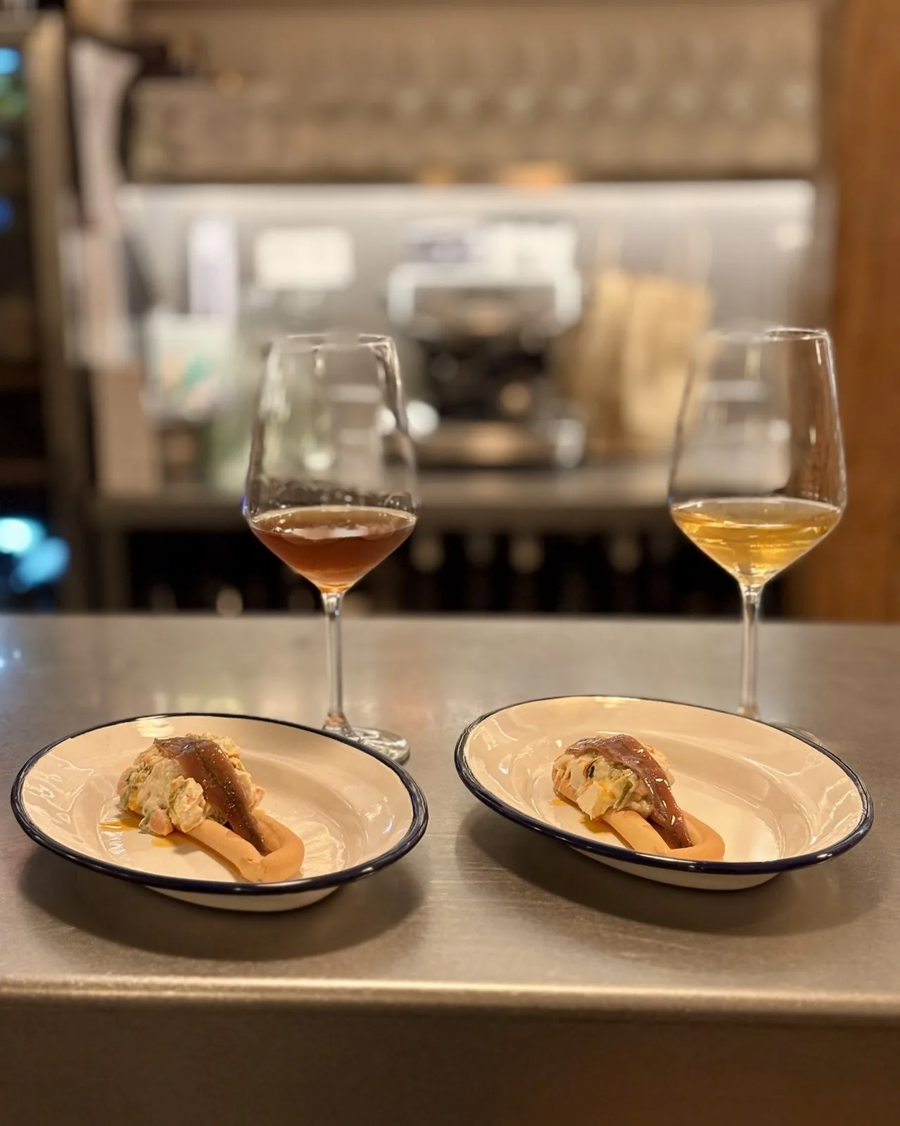 Two glasses of wine and two small plates of tuna bites on a steel bar counter