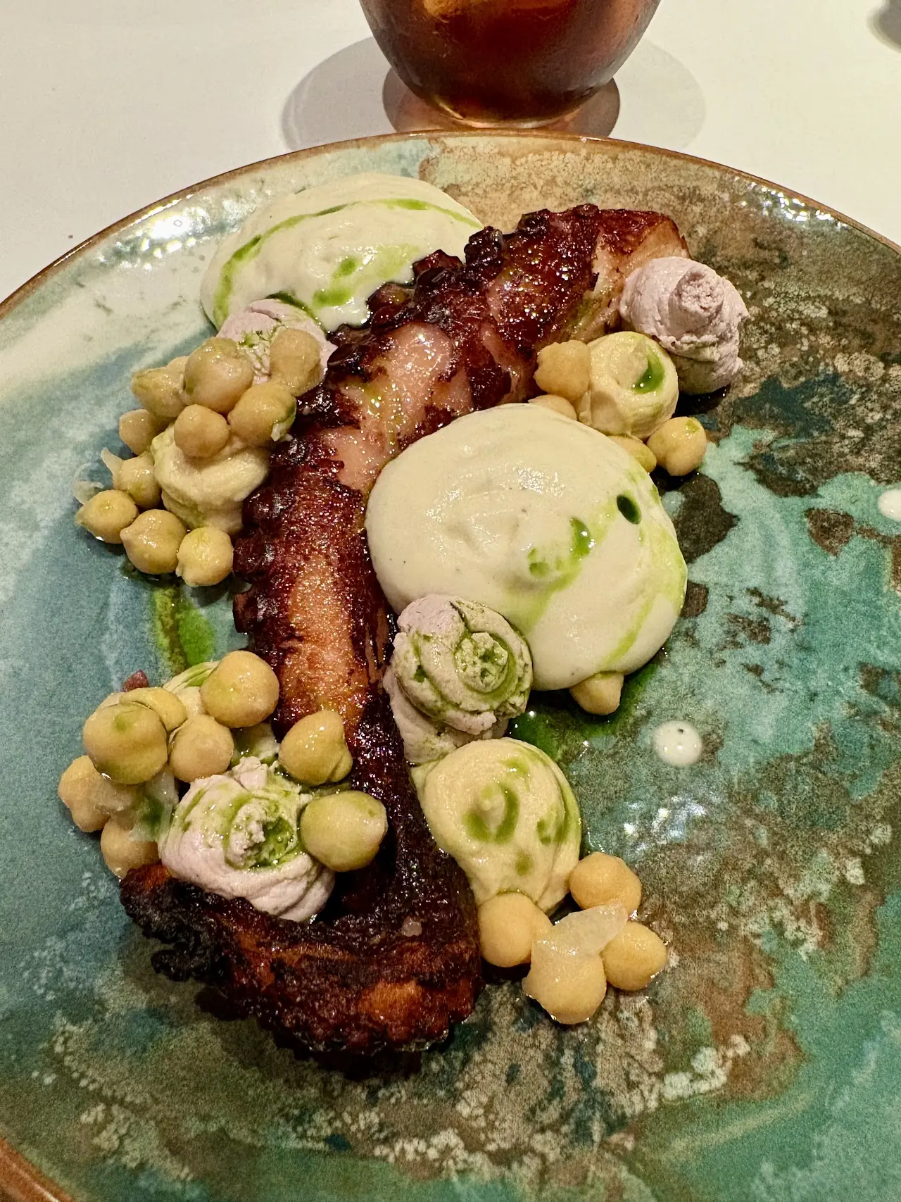 Charred octopus with chickpeas and a light sauce on a teal plate.