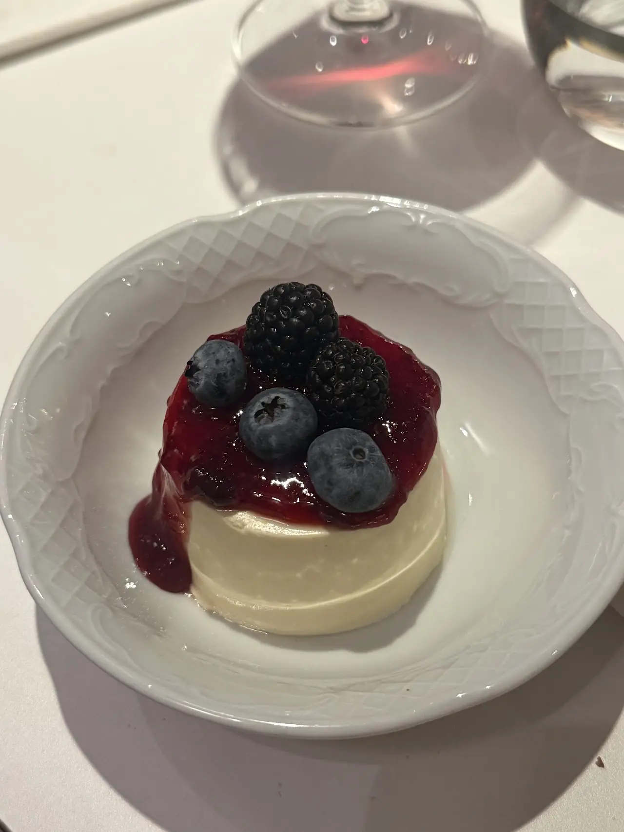 A domed panna cotta topped with blackberries and blueberries on a textured white plate.