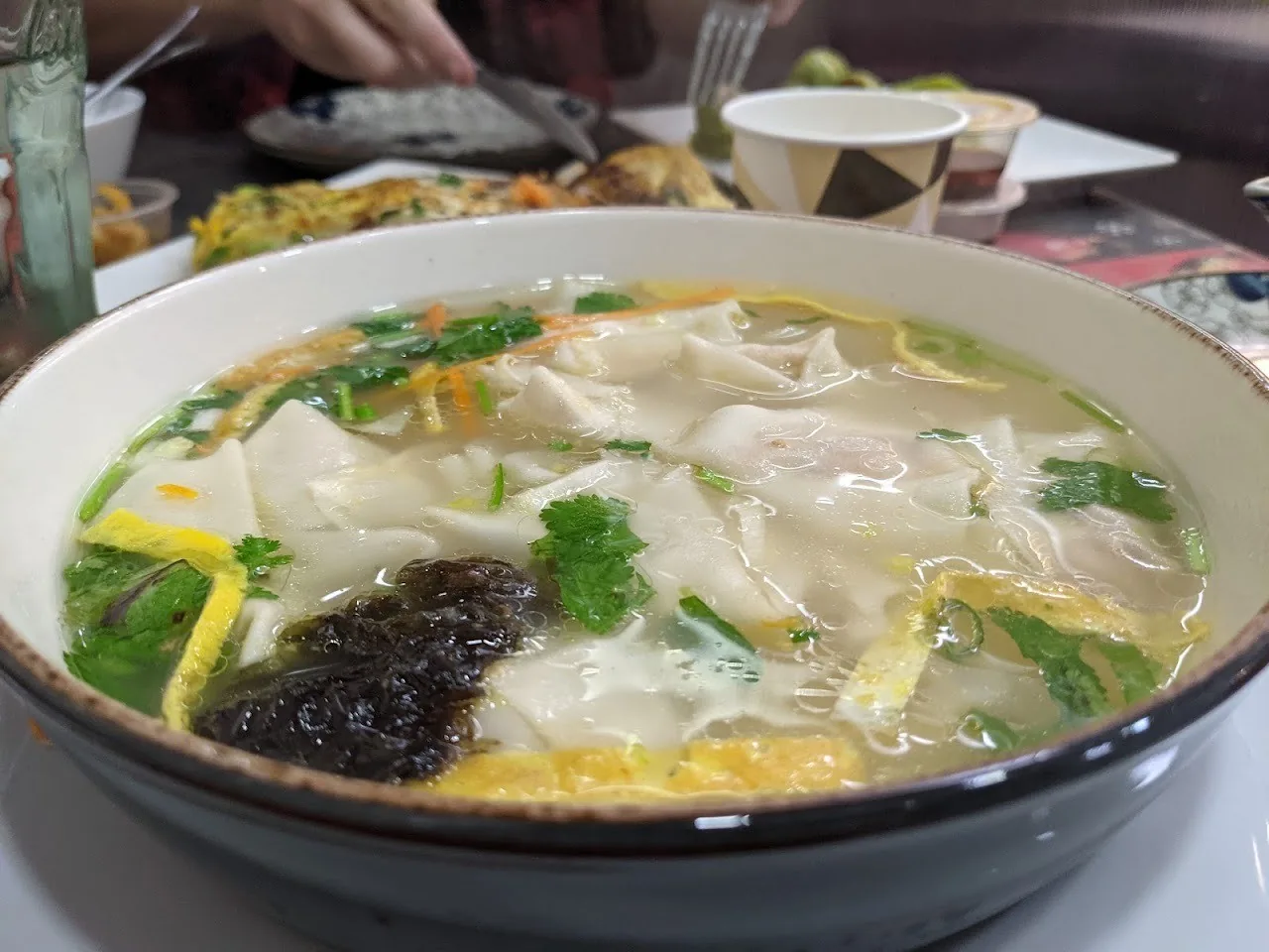 A bowl of wonton soup with herbs and seaweed