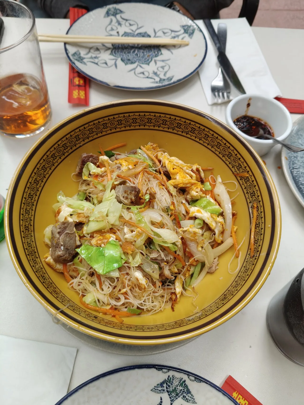 A yellow patterned plate of stir-fried noodles with vegetables and meat