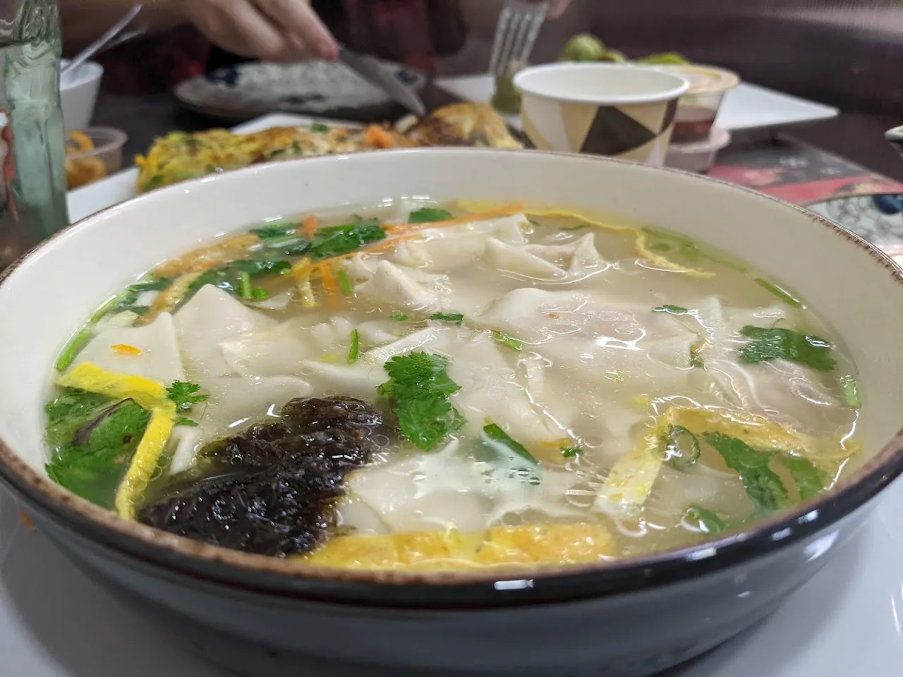 A bowl of soup with wontons, egg ribbons, and herbs
