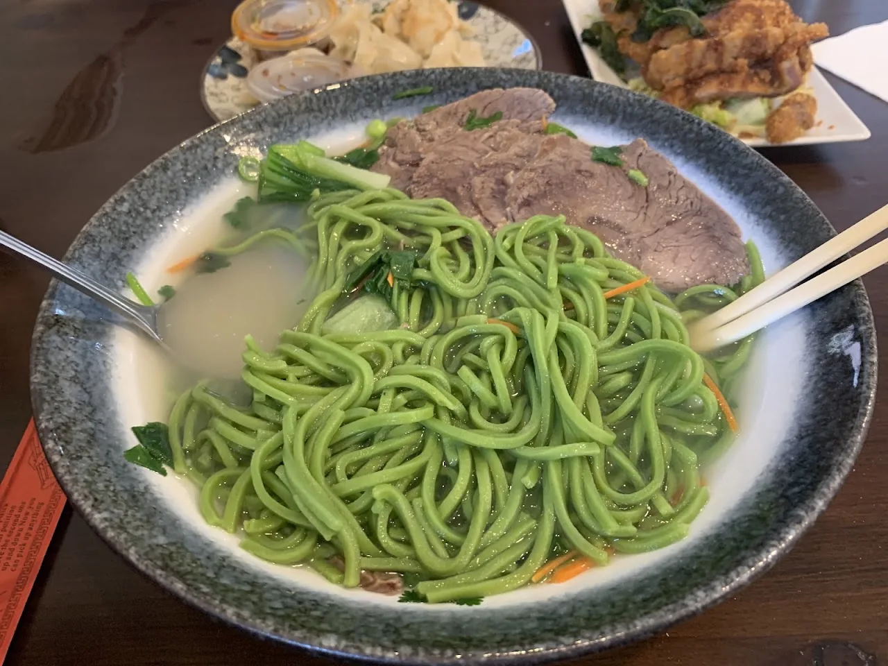 A bowl of green noodle soup with sliced meat