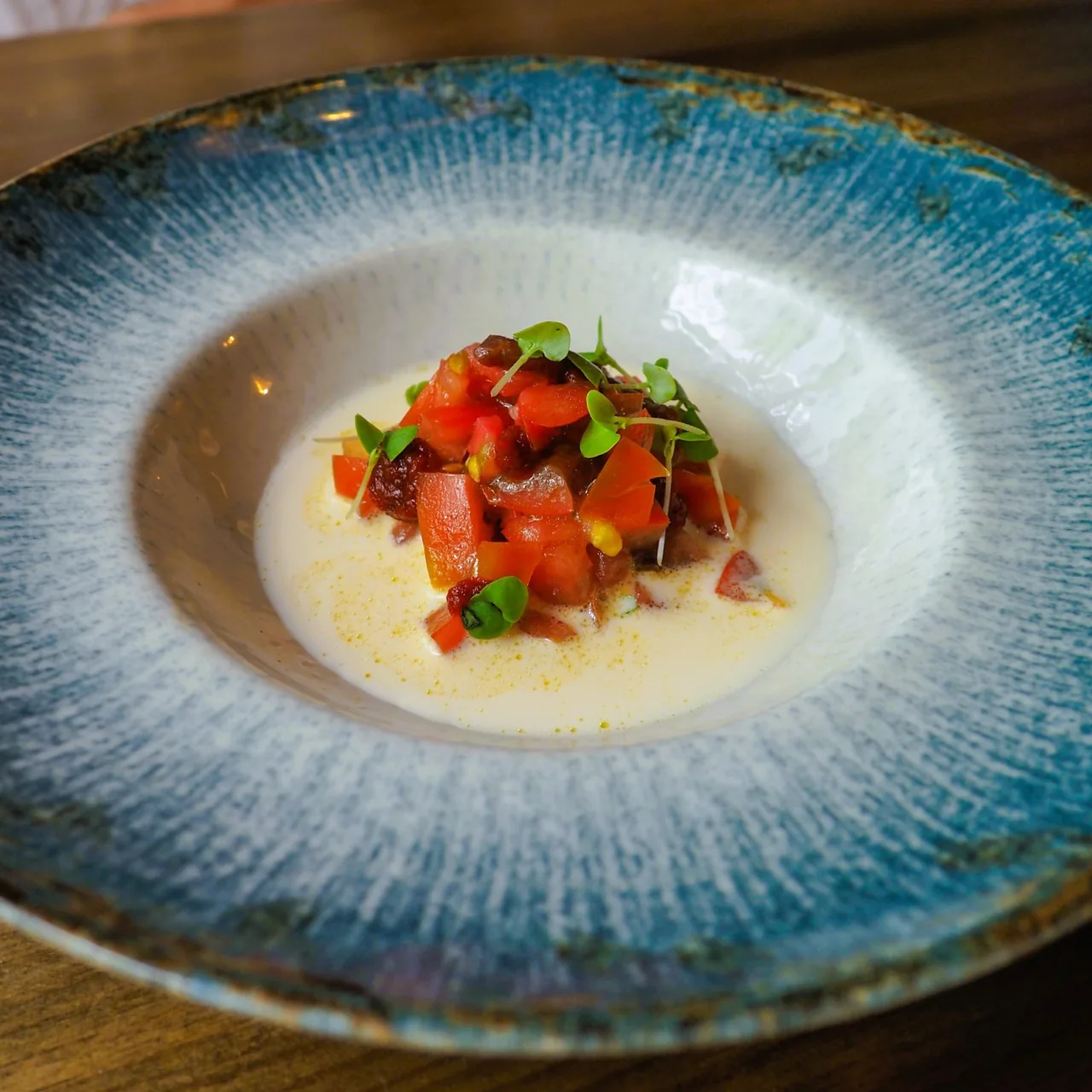 A blue-rimmed bowl of white cream topped with chopped tomato