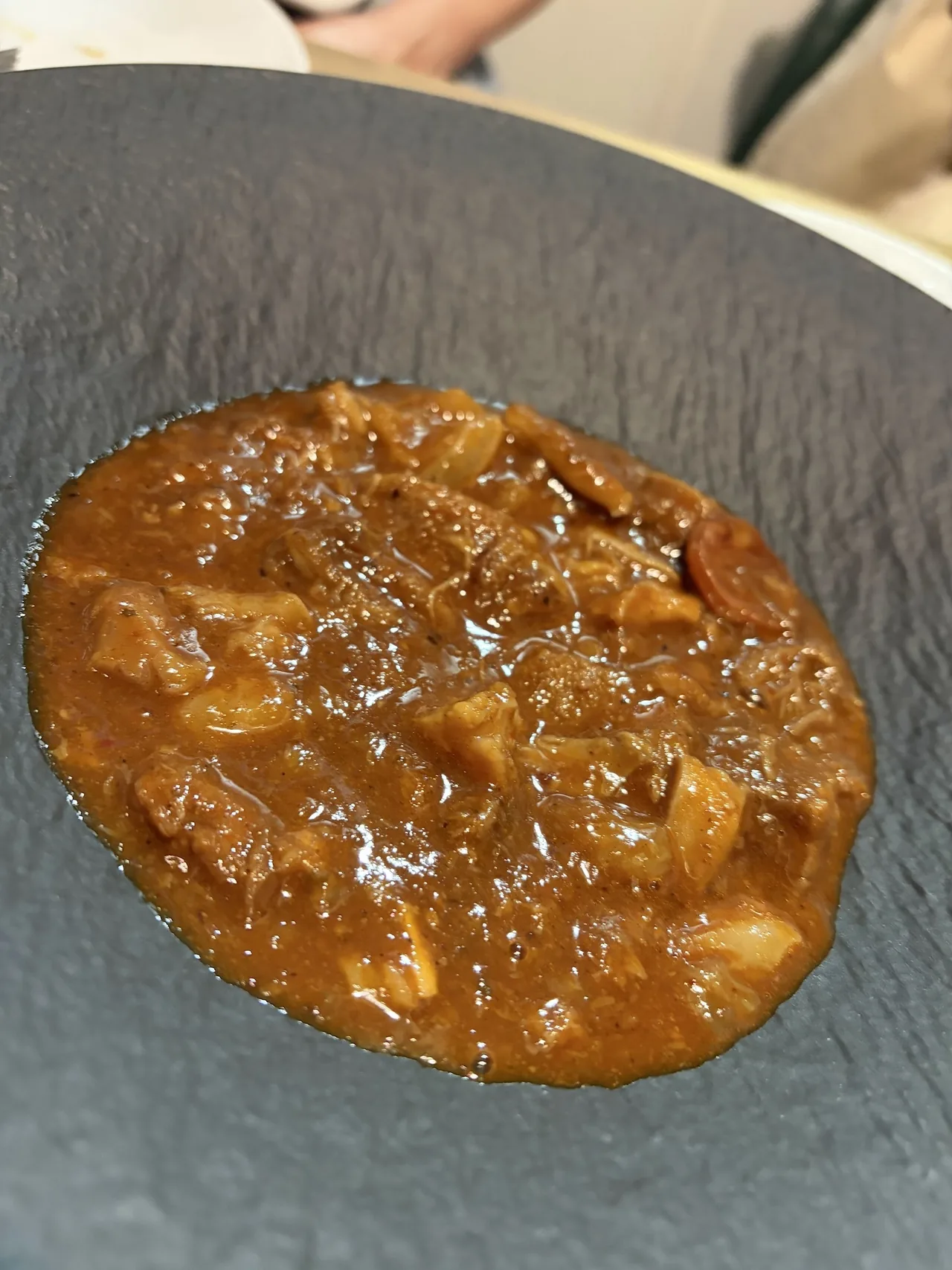 Tripe stew in a thick red-brown sauce on a dark slate-textured plate