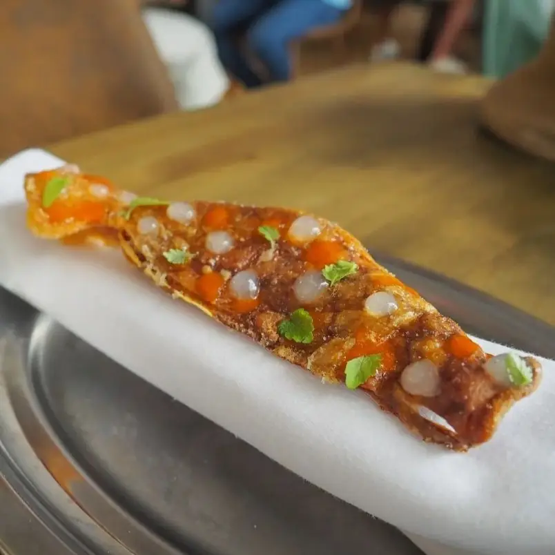 Thin elongated crispy tuile topped with small toppings, served draped on a napkin