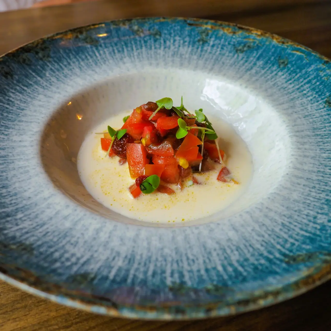 Diced tomato salad with microgreens over a pale creamy broth in a blue-glazed bowl