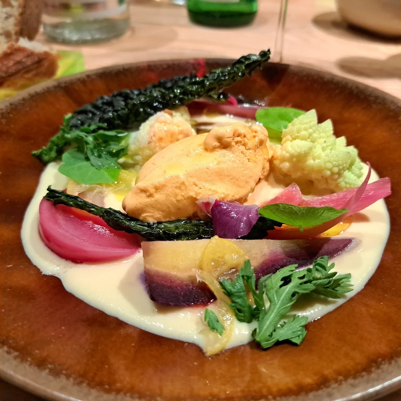 A plate of roasted vegetables and greens on a cream sauce in a brown bowl