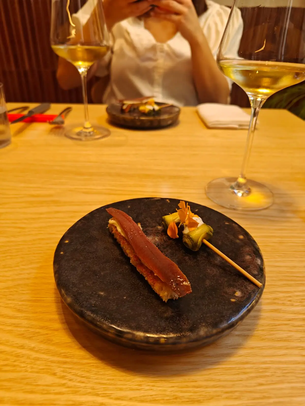 Anchovy toast and a vegetable skewer served on a dark round plate