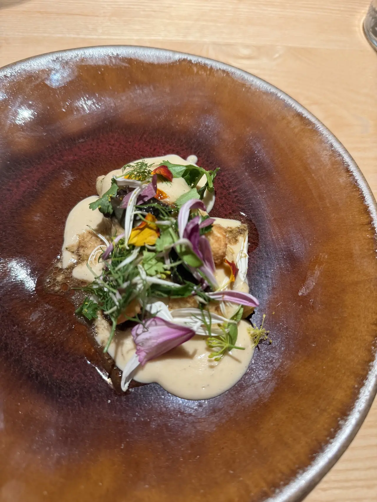 Plated dish with creamy sauce, herbs and edible flowers on a dark ceramic plate