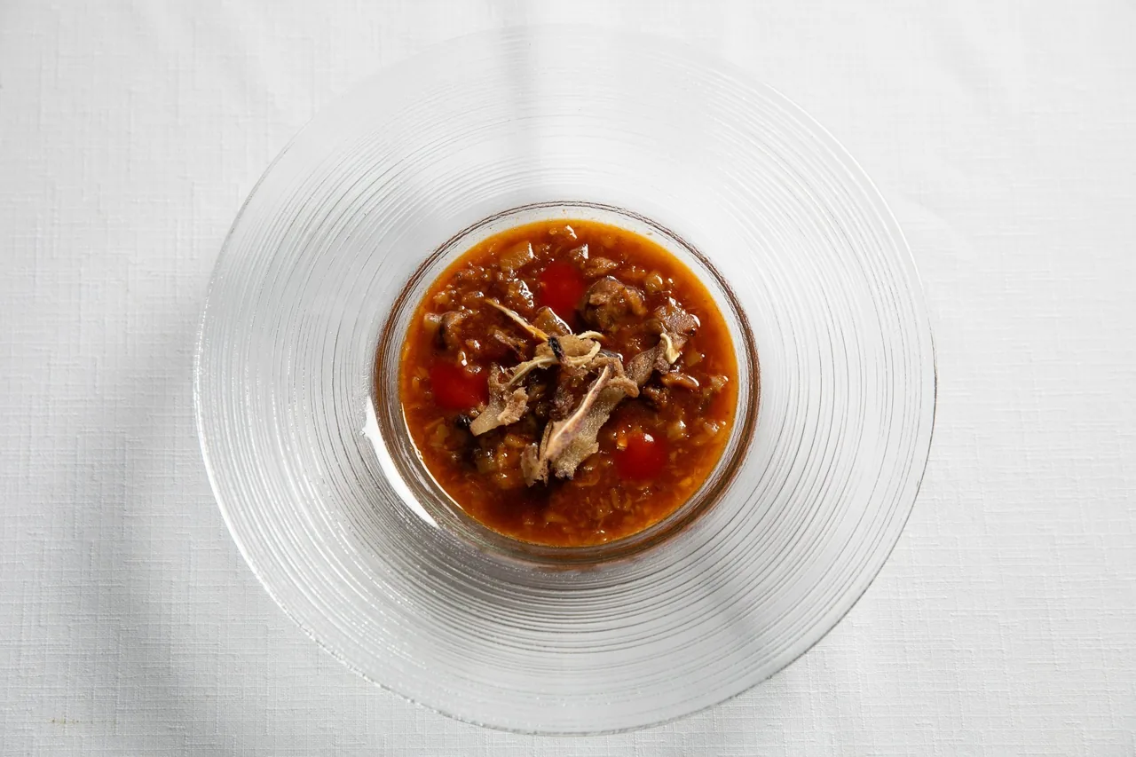 A clear glass bowl of a red-brown stew with shredded meat