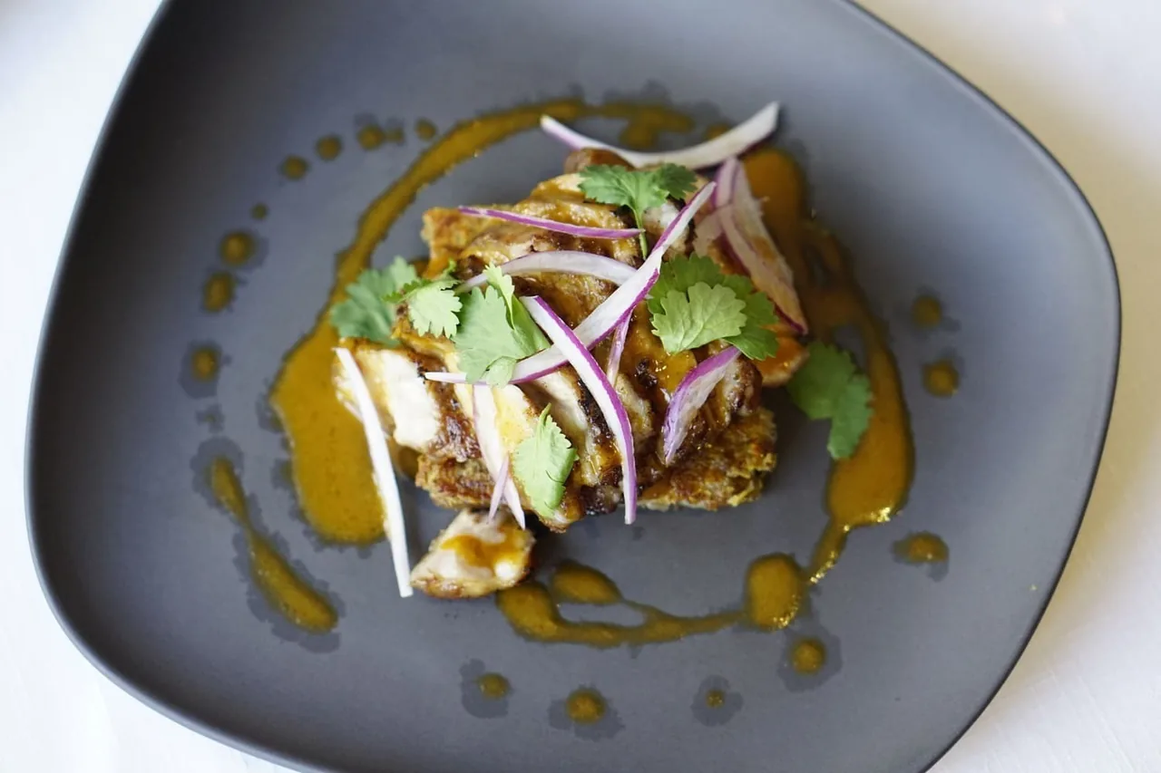 A dark grey plate holding a chopped dish topped with red onion and orange sauce
