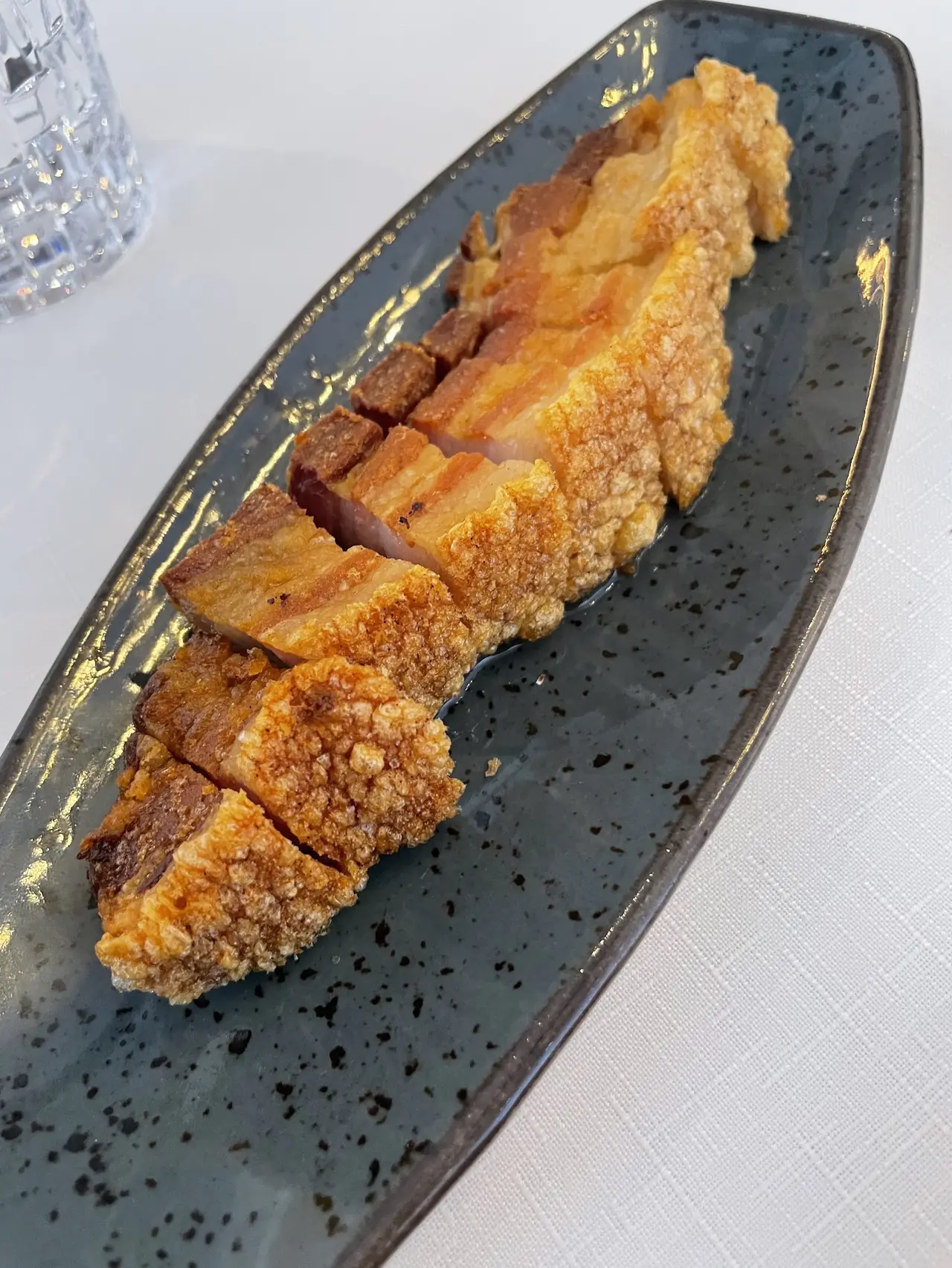 Sliced crispy-skin pork belly pieces on a long dark speckled plate