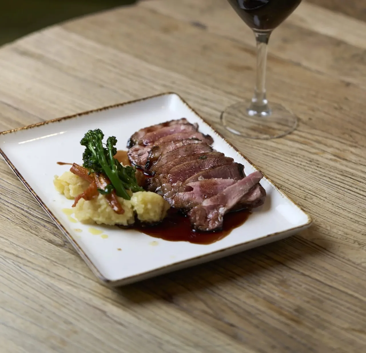 Slices of cooked meat with a sauce on a square white plate on a wooden table