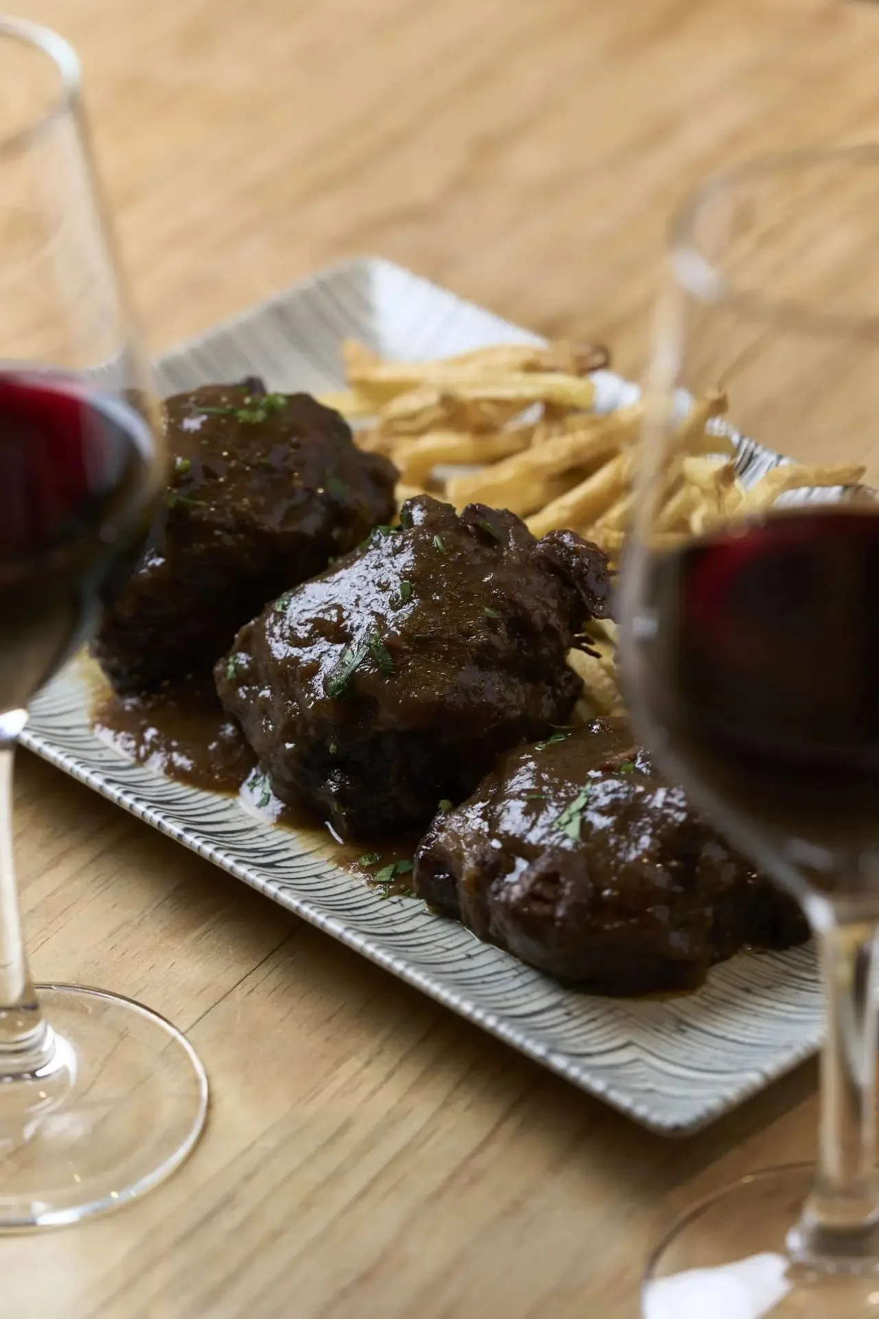 Pieces of braised meat in dark sauce with fries on a white plate