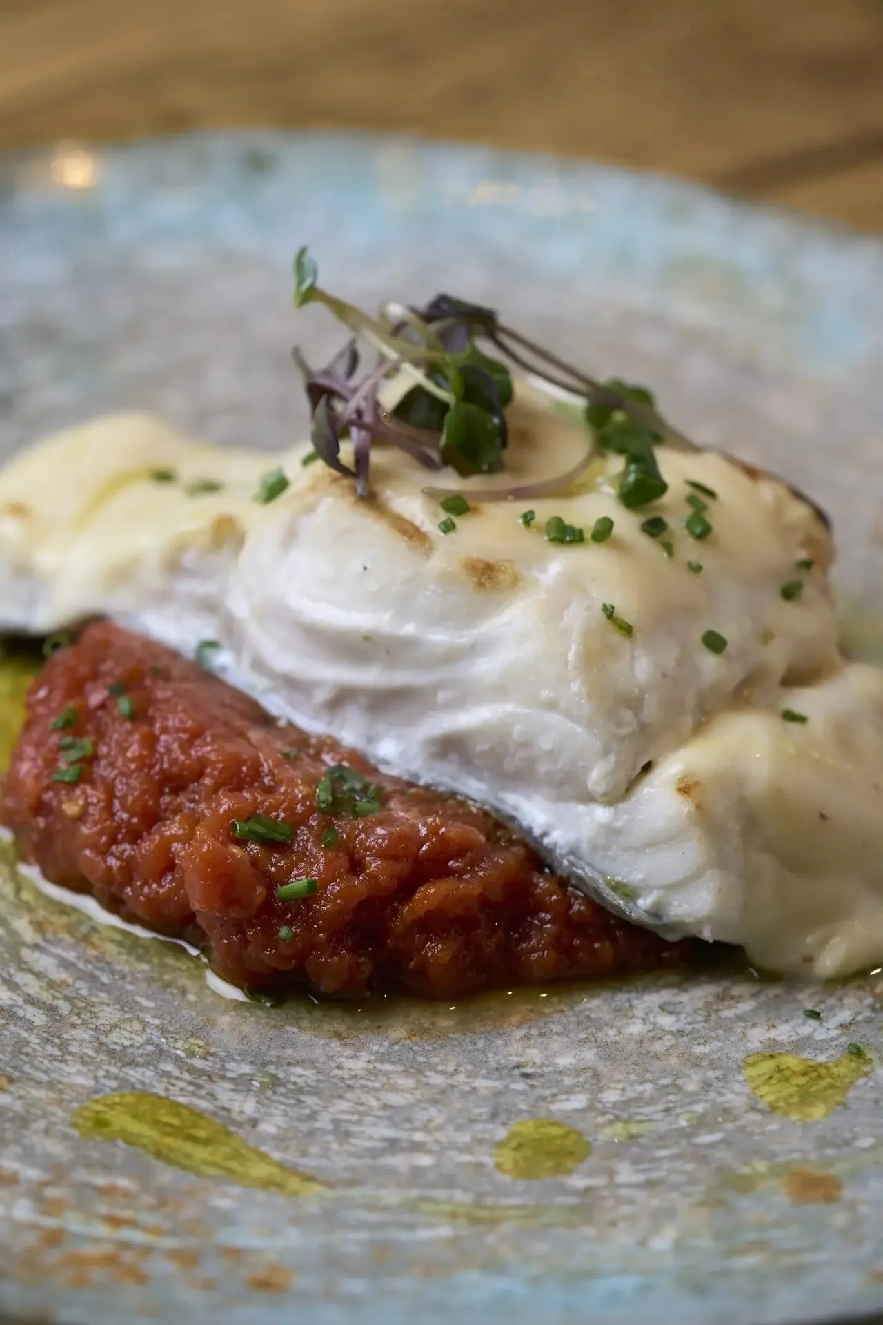 A slab of white creamy topping over tomato sauce on a grey plate