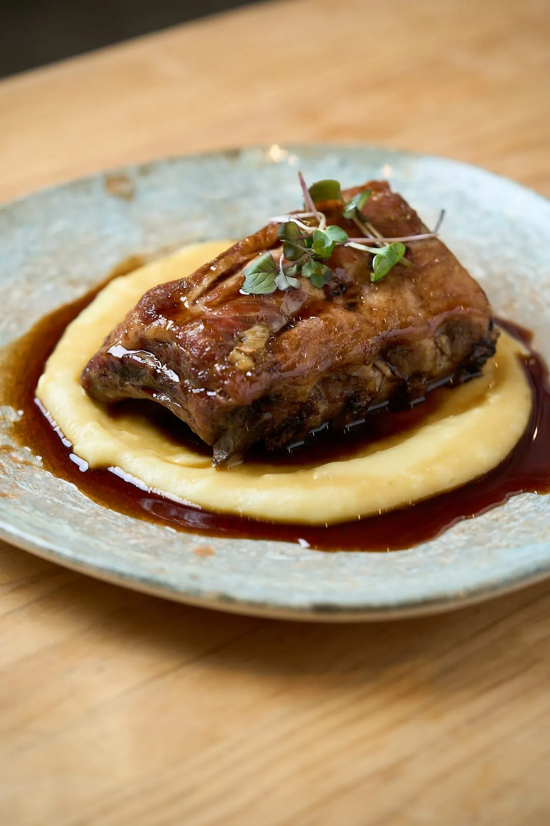 A braised rib of meat on a bed of creamy polenta in a blue-grey bowl
