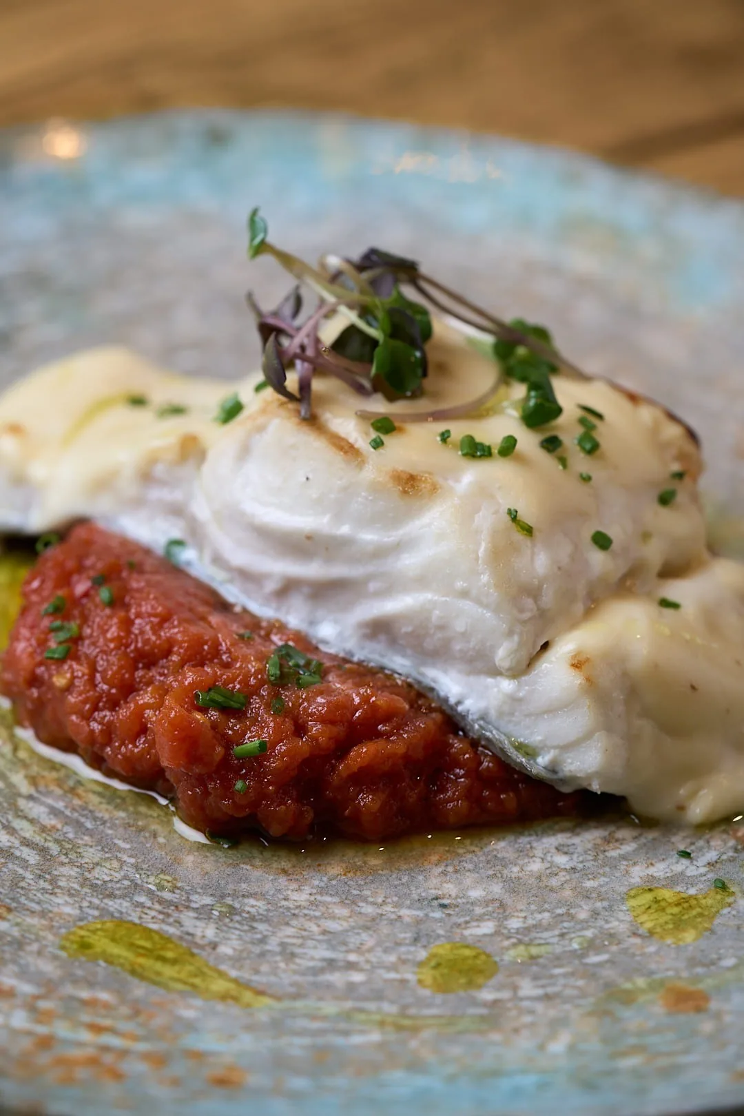 A piece of white fish with foam on a tomato sauce in a grey-blue plate