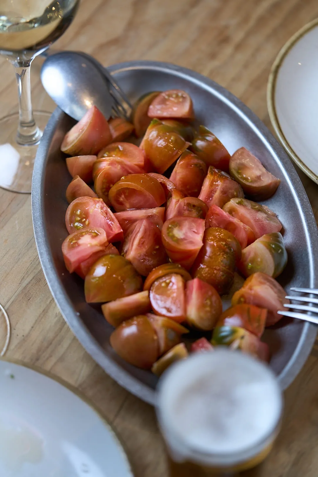 An oval metal dish of chopped tomatoes with a glass of beer beside it
