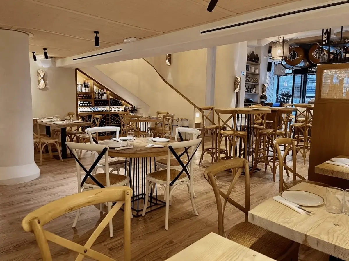 A bright restaurant interior with wooden tables and chairs and a staircase