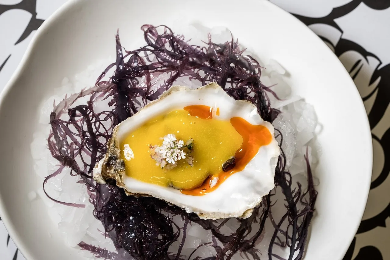 An oyster on a bed of purple seaweed with an orange topping on a white plate