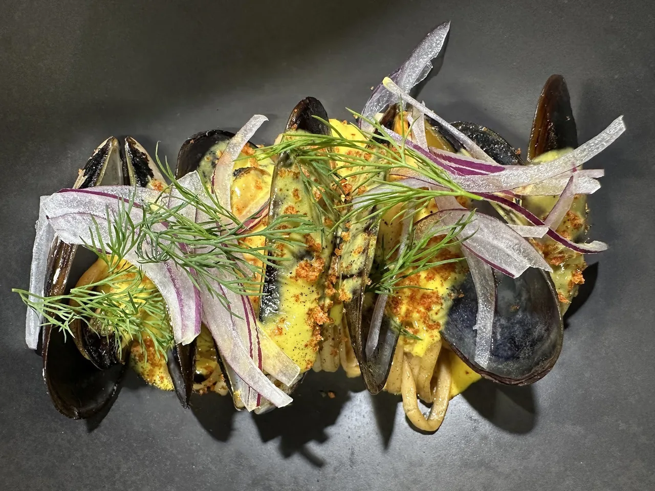 A dark bowl of mussels topped with thin sliced onion and herbs