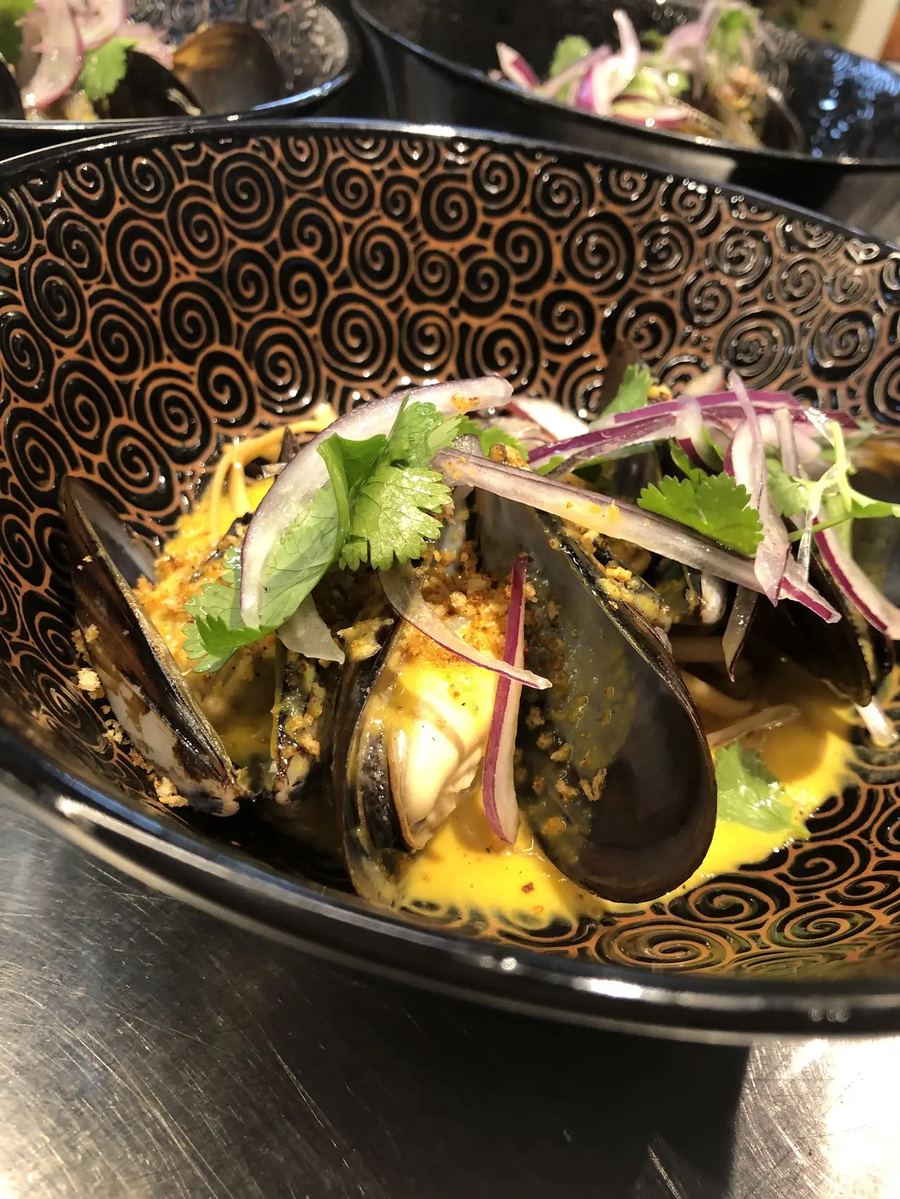 Mussels in yellow curry broth topped with pickled red onion and coriander in a patterned bowl