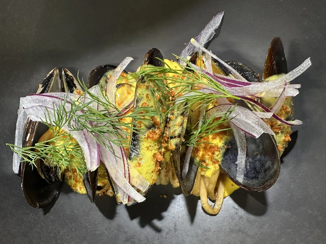 Mussels with noodles in yellow sauce topped with dill and pickled red onion, overhead view