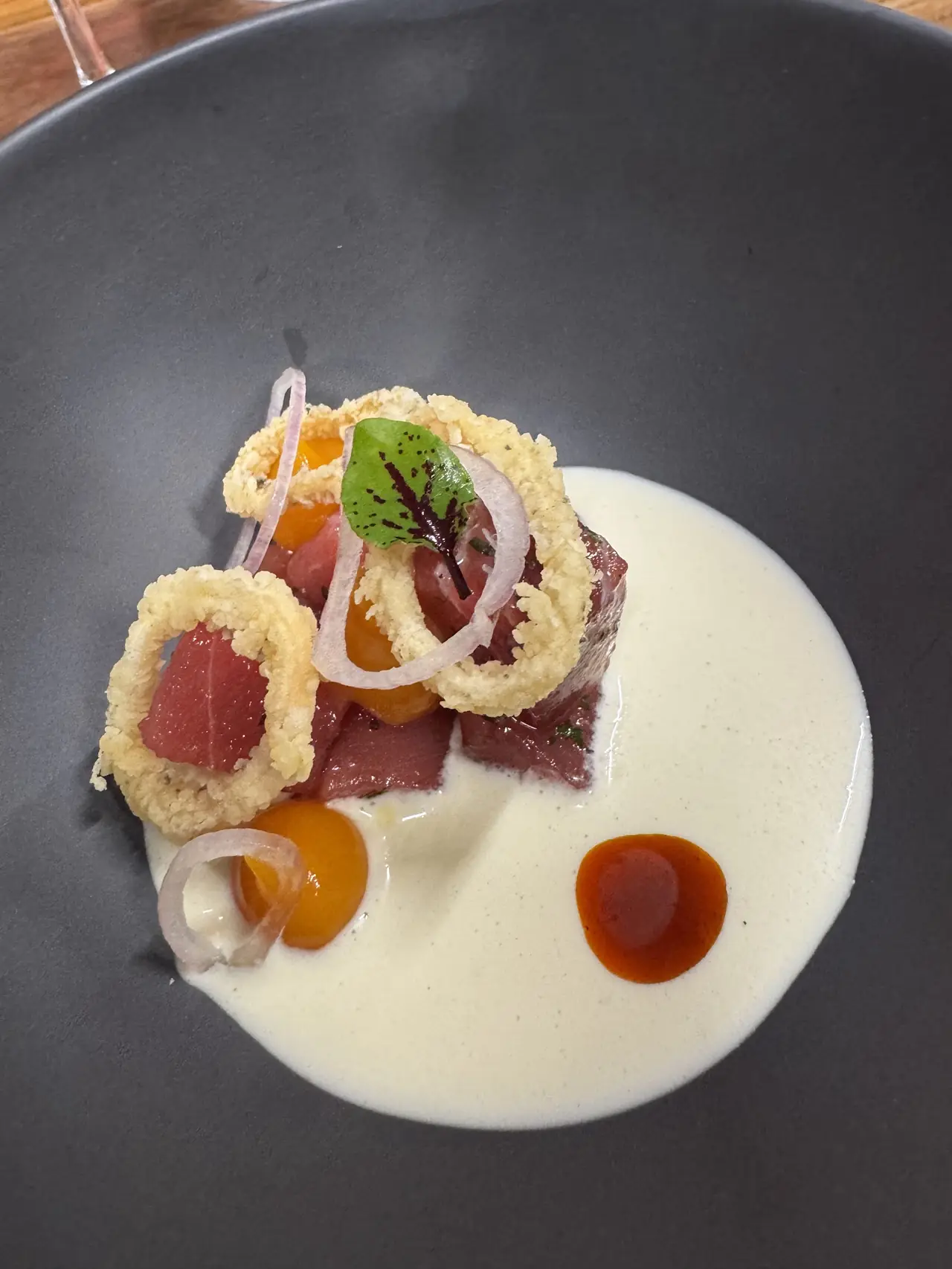 Tuna tartare with crispy onion rings and citrus over a cream sauce in a black bowl