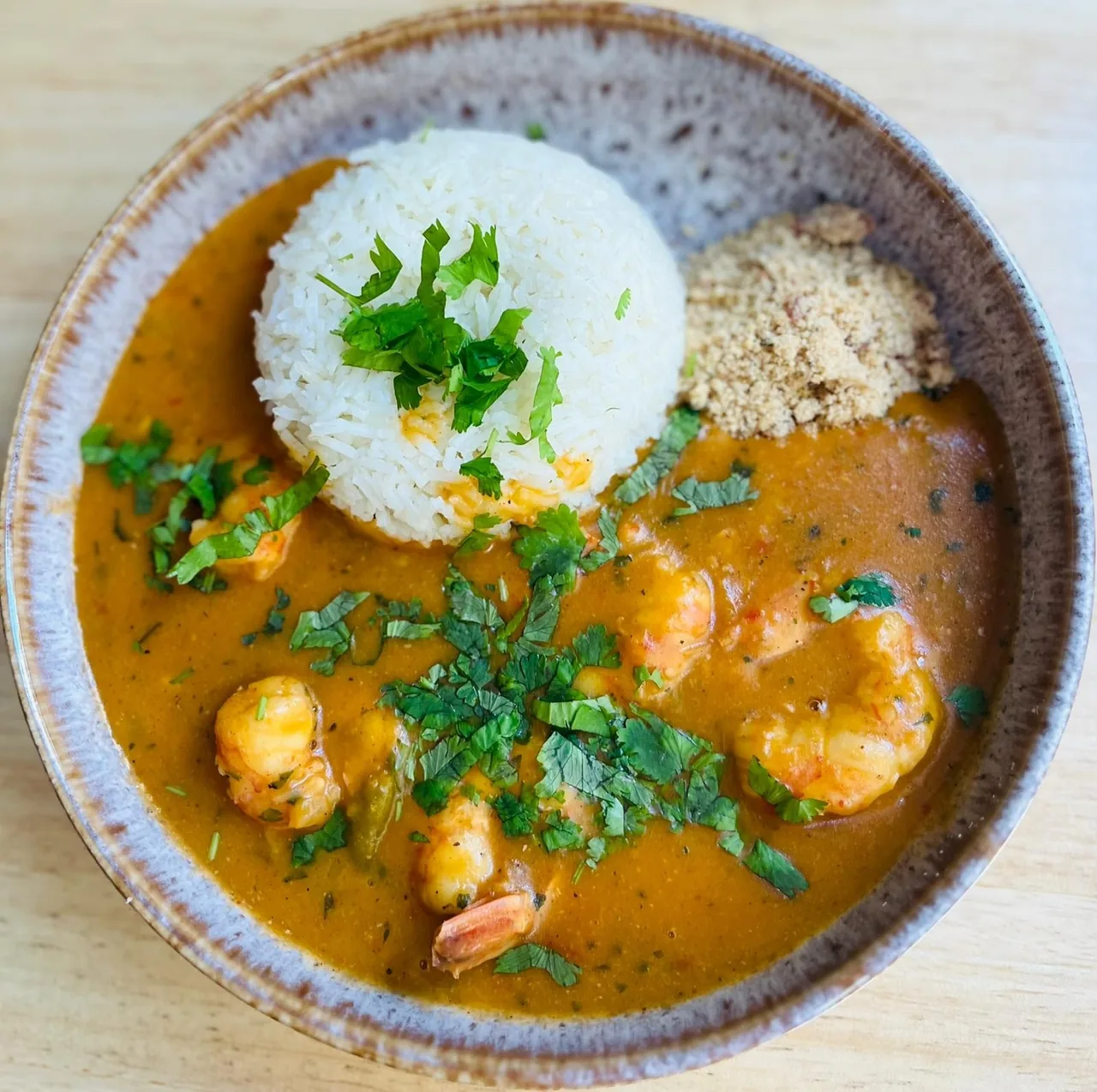 A bowl of shrimp in an orange sauce with white rice and a pile of toasted flour
