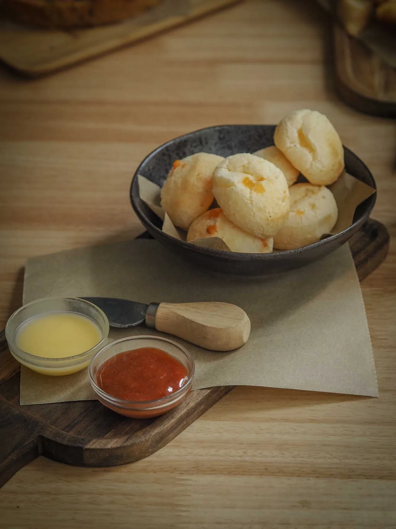A dark bowl of small cheese bread balls with two dipping sauces
