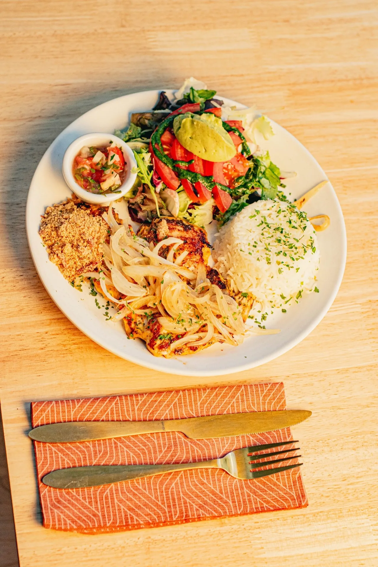 A plate of grilled meat, rice and salad on a wooden table