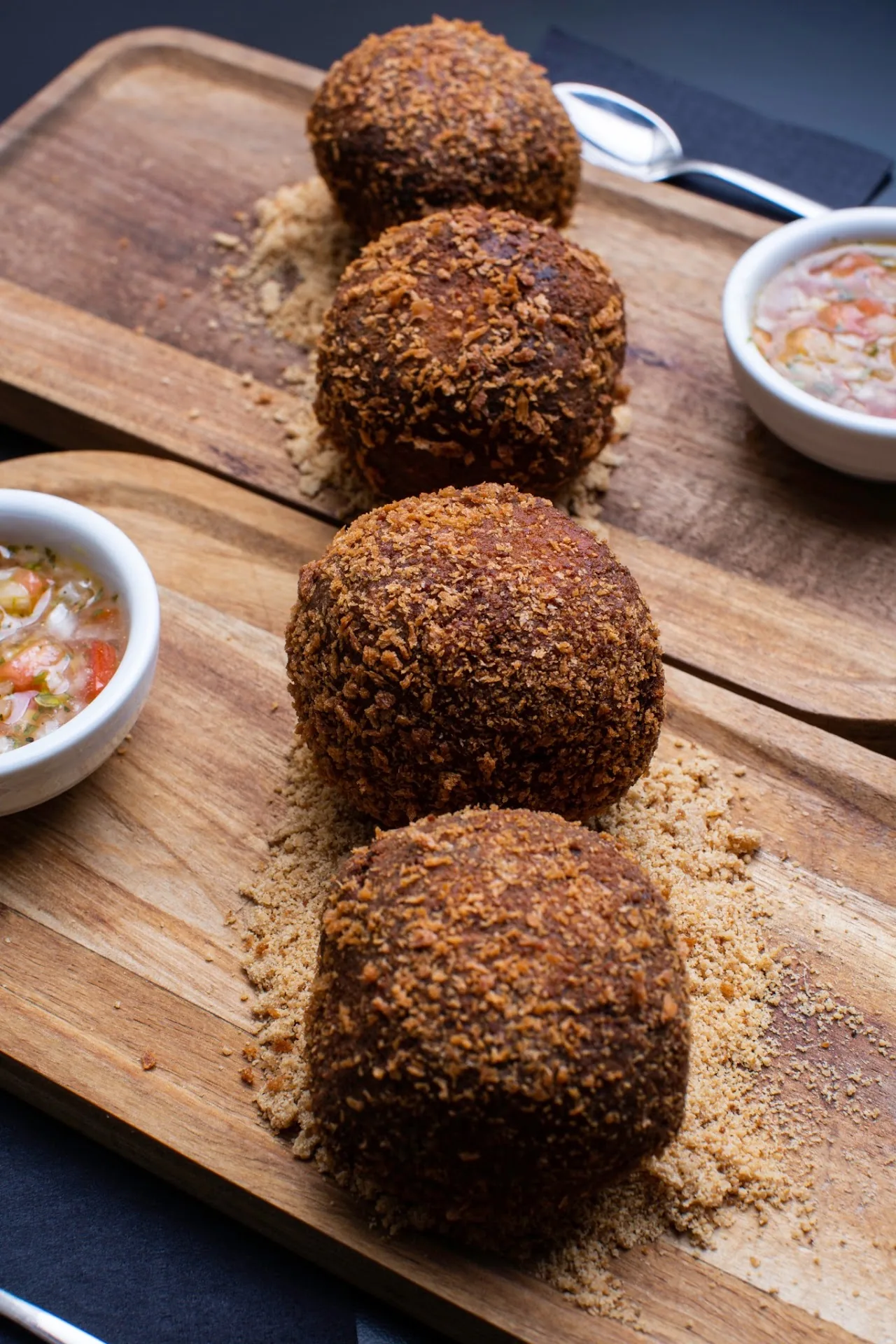 Four breaded fried croquette balls on a wooden board with dipping sauces