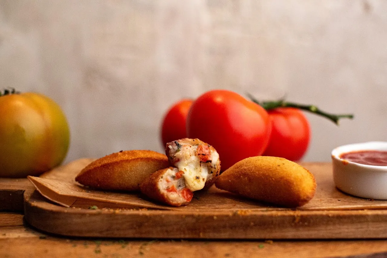 Golden fried pastries (Brazilian-style empanadas) on a board with fresh tomatoes