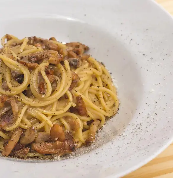 Bowl of spaghetti alla gricia with crisp guanciale and black pepper in a white bowl