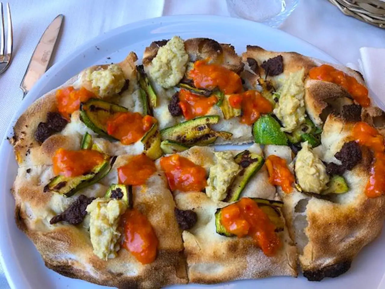 Flatbread pizza topped with roasted zucchini, tomato sauce and dollops of fresh white cheese