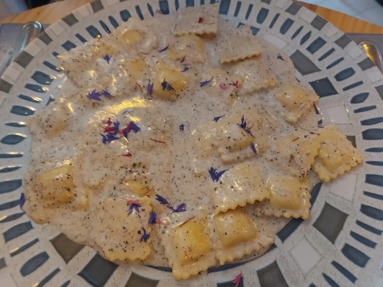 Square ravioli in a cream sauce garnished with edible purple flowers.