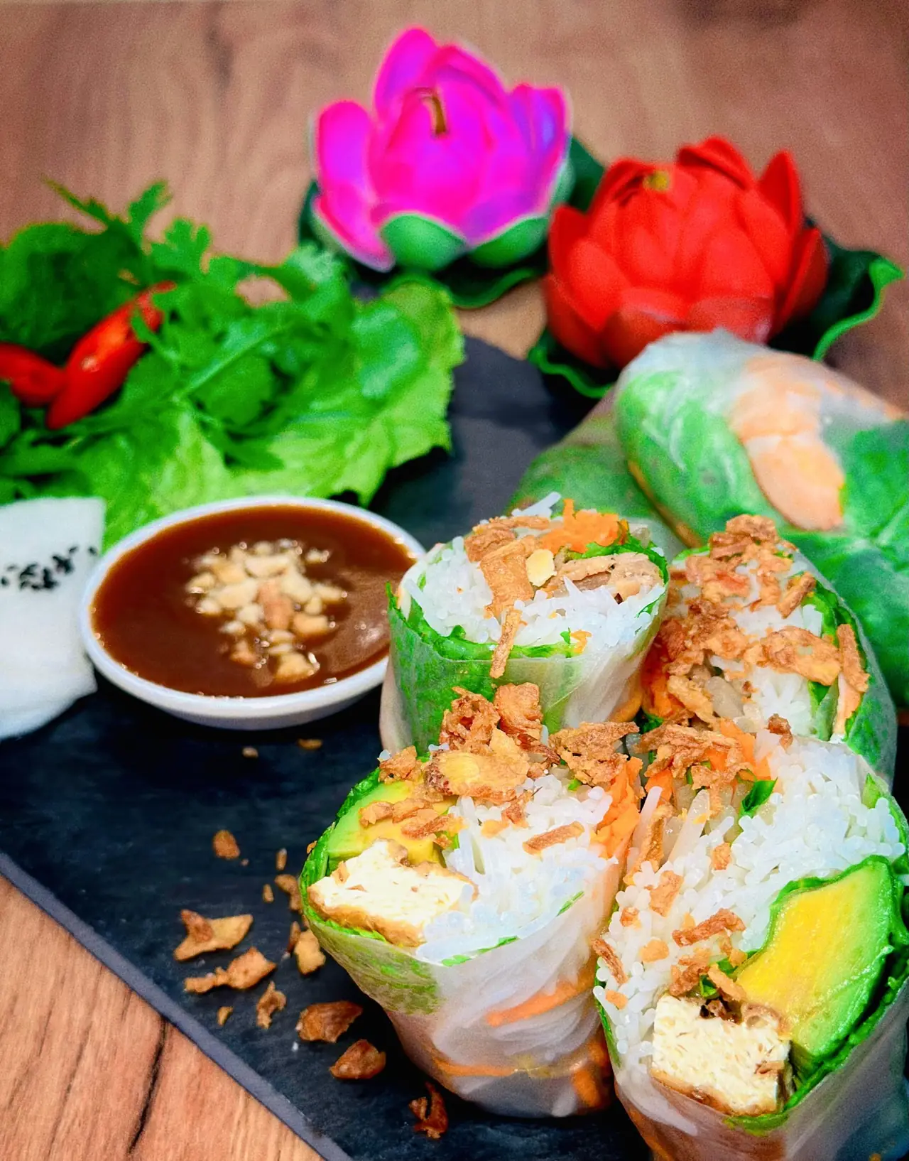 Fresh rice paper rolls filled with tofu, avocado, rice, and vegetables, sliced open and topped with crispy shallots, served with peanut dipping sauce and herbs, Tutu Vietnamese Cuisine