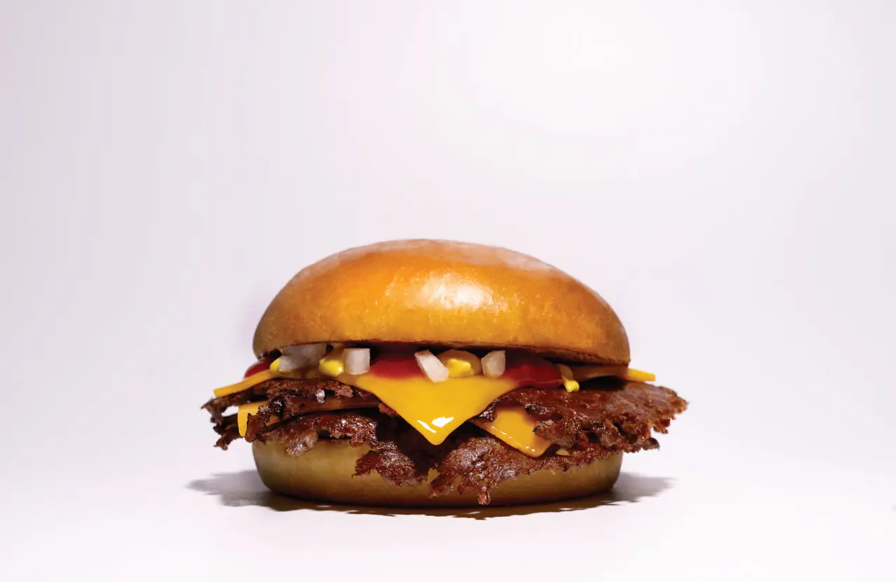 Side view of a smashed cheeseburger with melted American cheese, ketchup, mustard, and diced onion on a glossy brioche bun, Two Patties