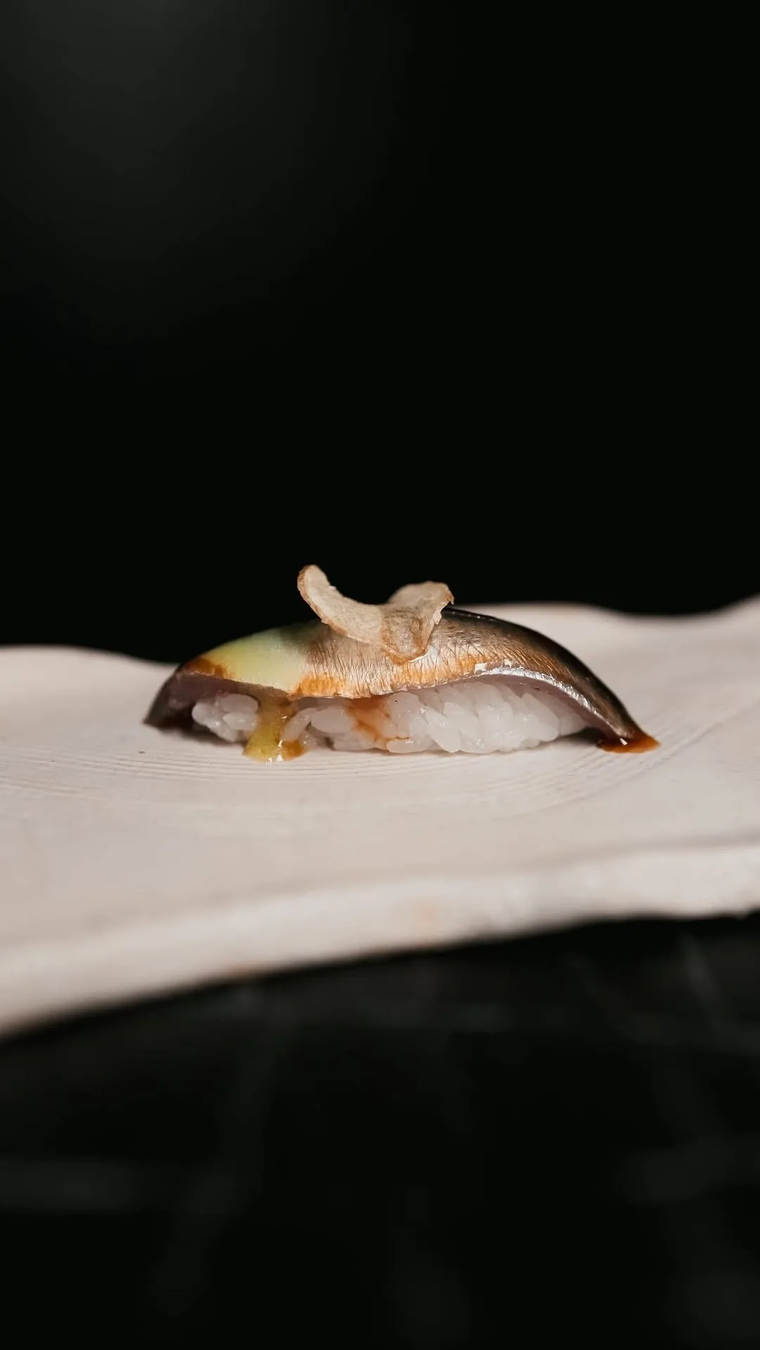 A single piece of nigiri on a pale ceramic plate against a dark background