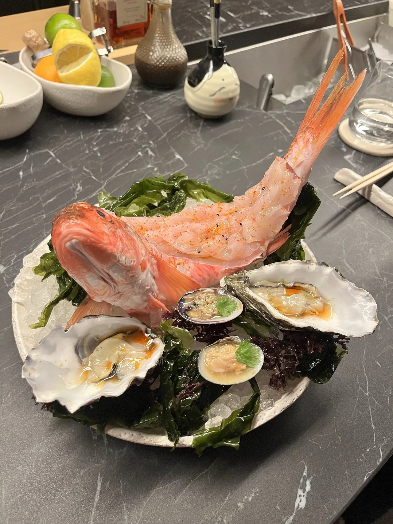 A sliced whole red fish standing on a bed of seaweed and ice with oysters and clams