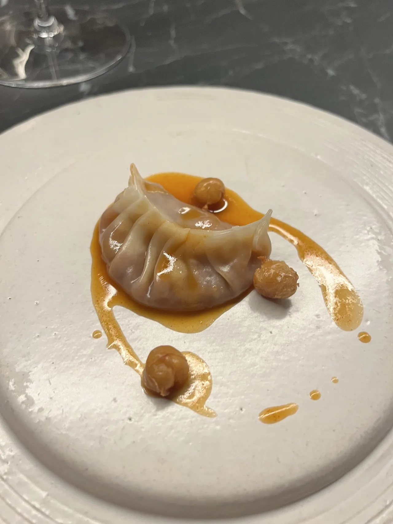 A dumpling in a light broth with small round nuts on a white plate