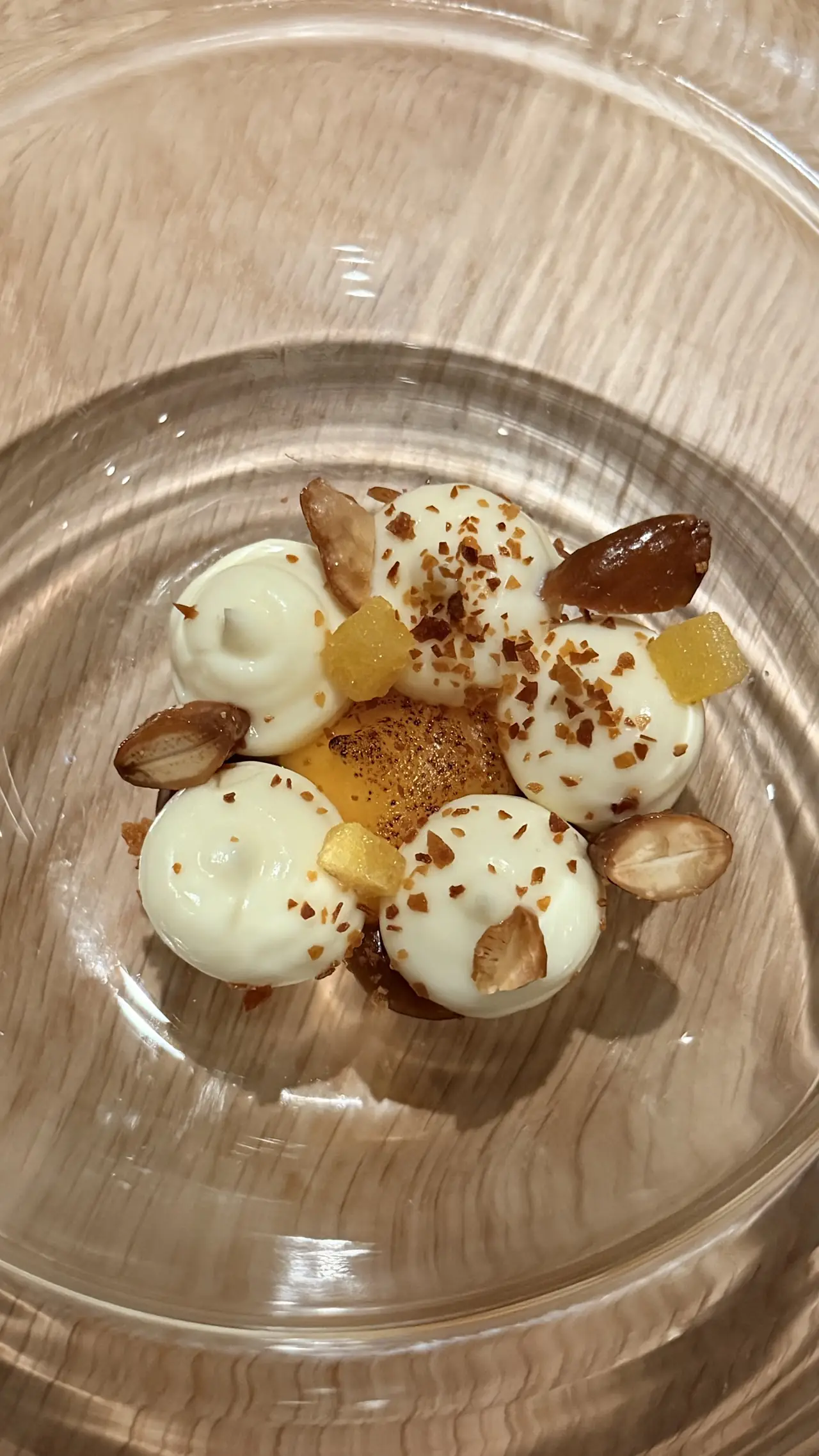 Dessert with white cream dollops, almonds, candied citrus cubes in glass bowl