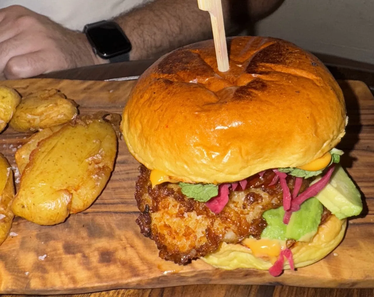 A burger with pickled toppings on a brioche bun, served with potatoes